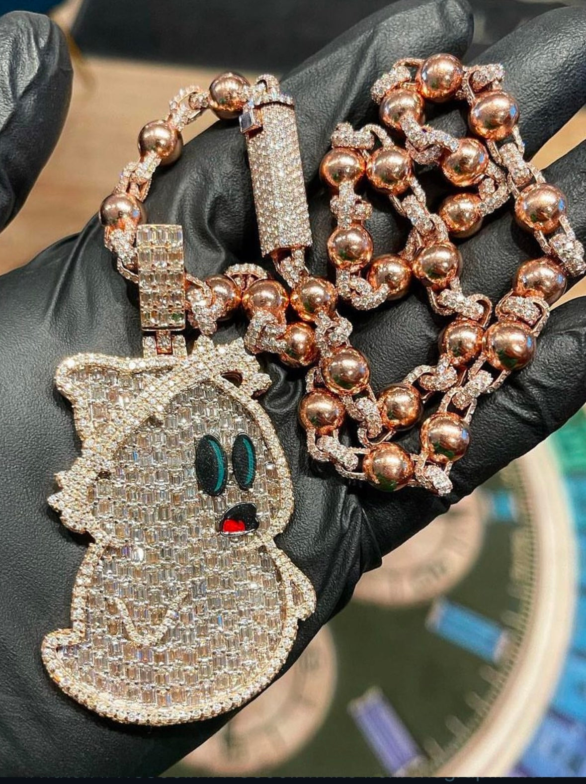 Gold ghost pendant and beaded chain held by a gloved hand