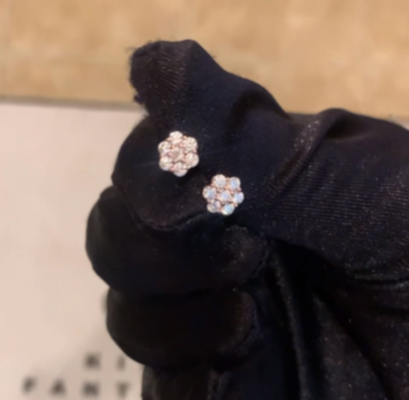 Pair of silver flower-shaped earrings held in a black glove against a neutral background