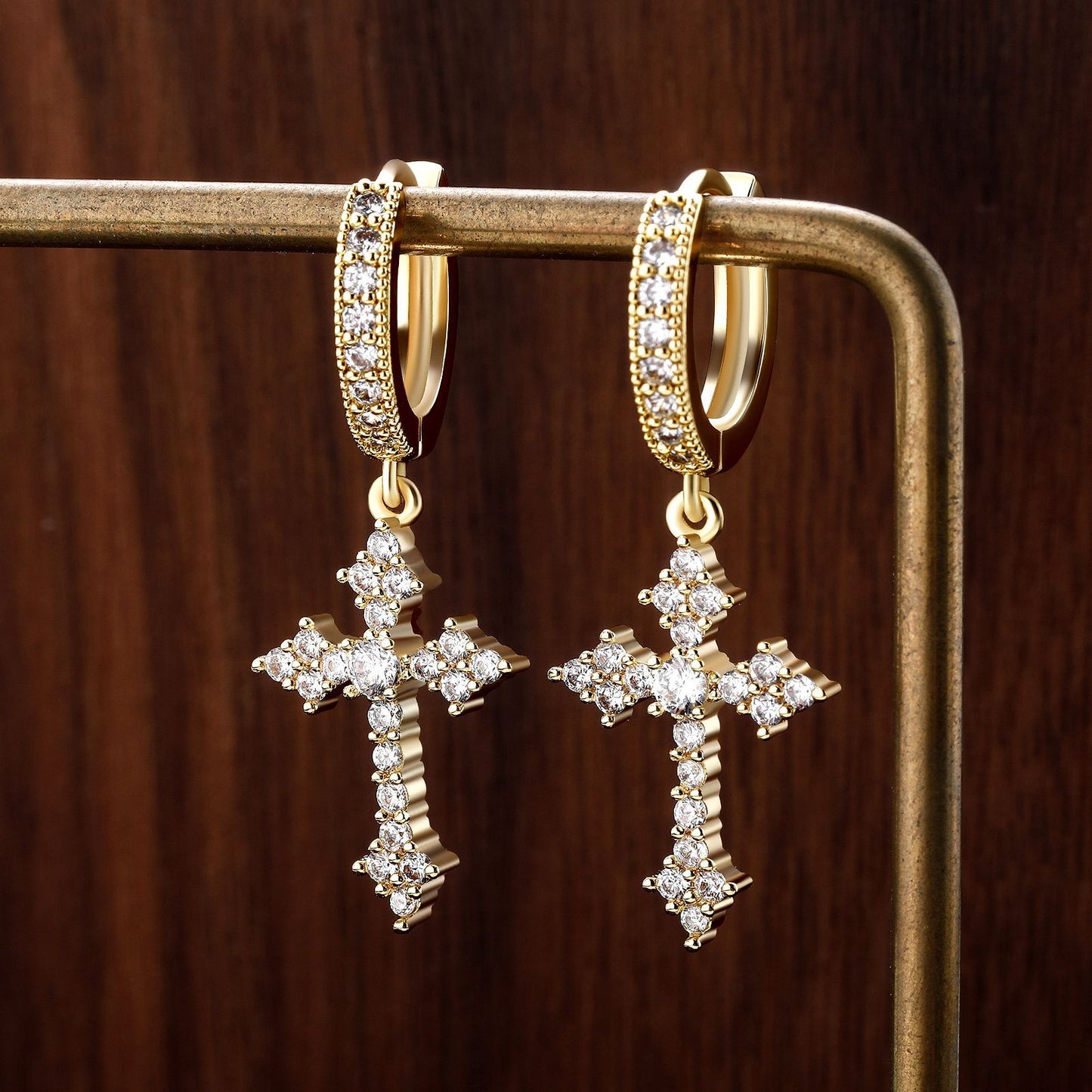 Gold cross earrings with diamond accents on a wooden surface