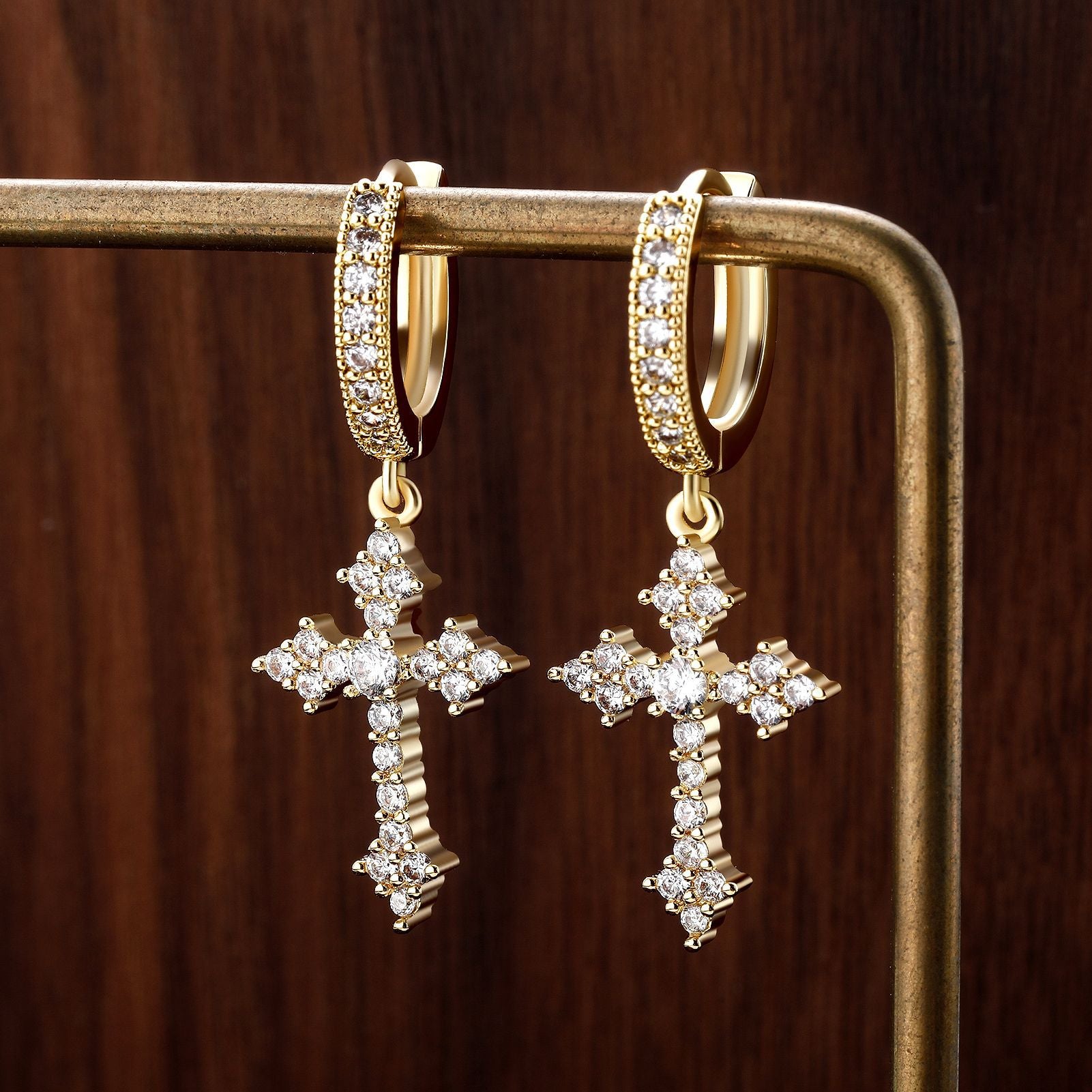 Gold cross earrings with diamond accents on a wooden surface