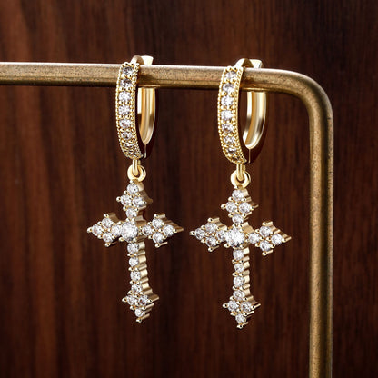 Gold cross earrings with diamond accents on a wooden surface